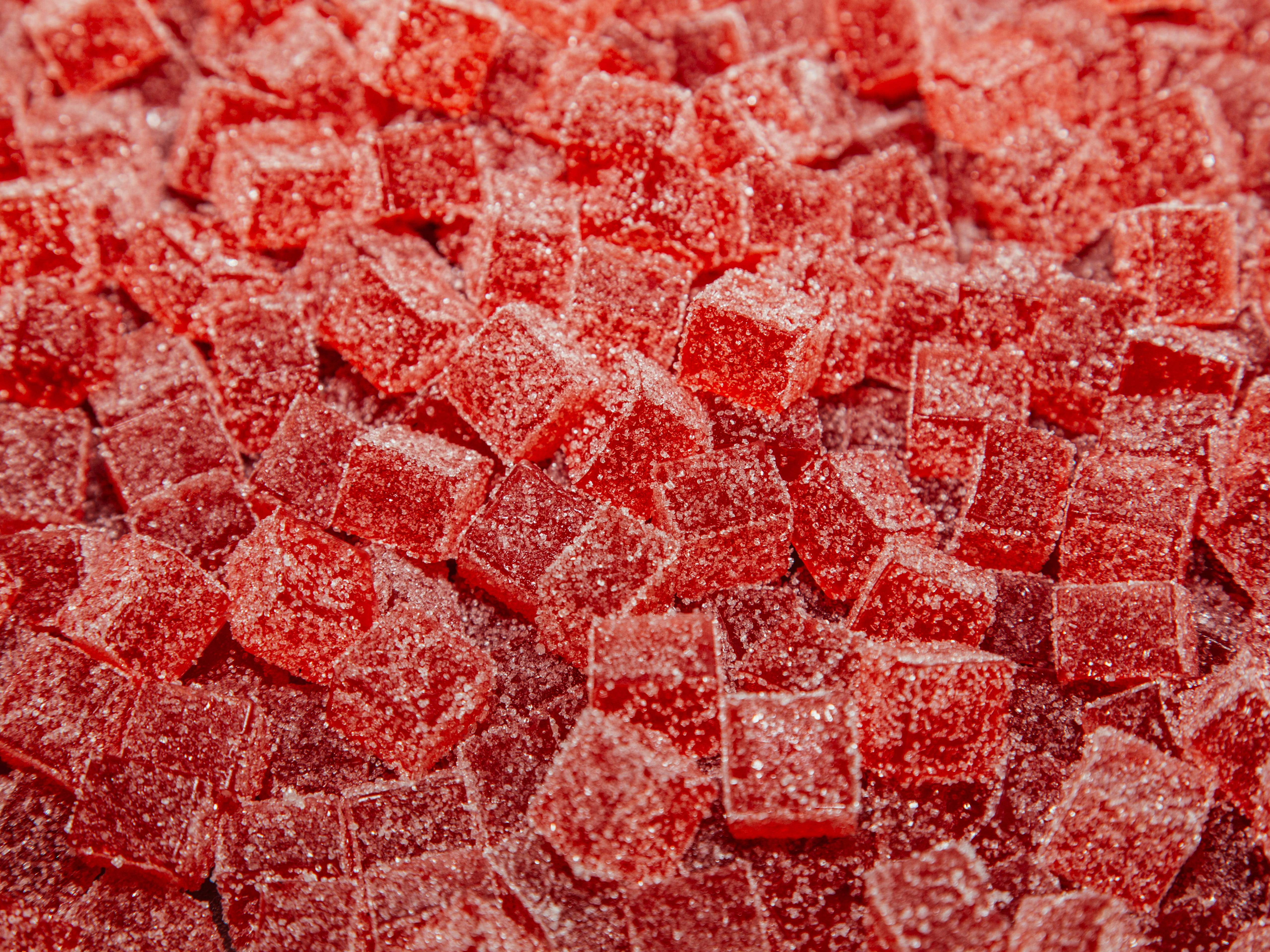 Close-up of numerous red sugar-coated gummy candy cubes.