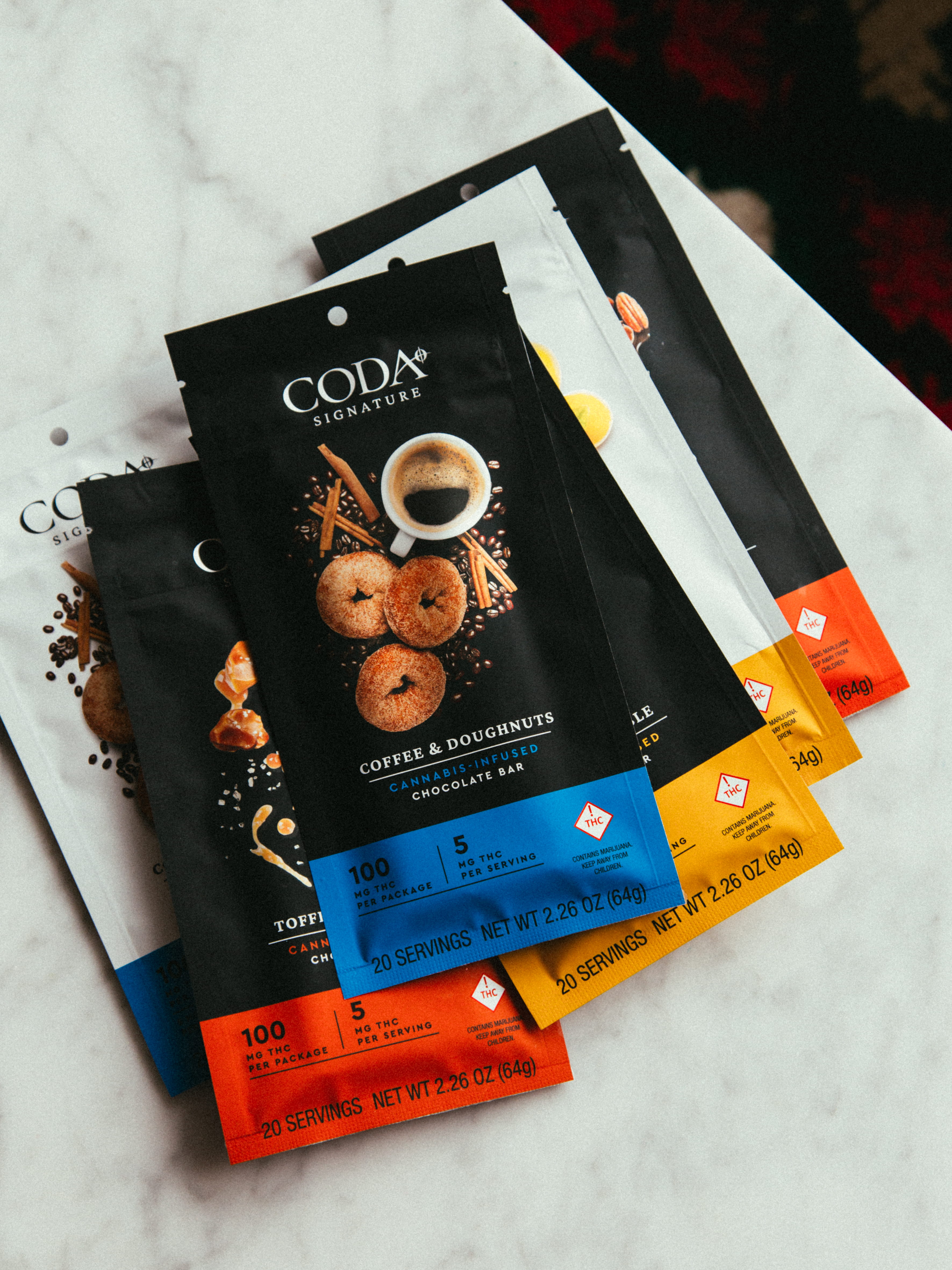 Packets of CODA Signature cannabis-infused chocolate bars in assorted flavors arranged on a marble surface.