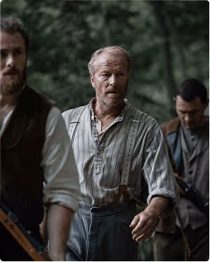 Three men in vintage clothing standing outdoors in a wooded area, with the central older man wearing suspenders and a striped shirt.