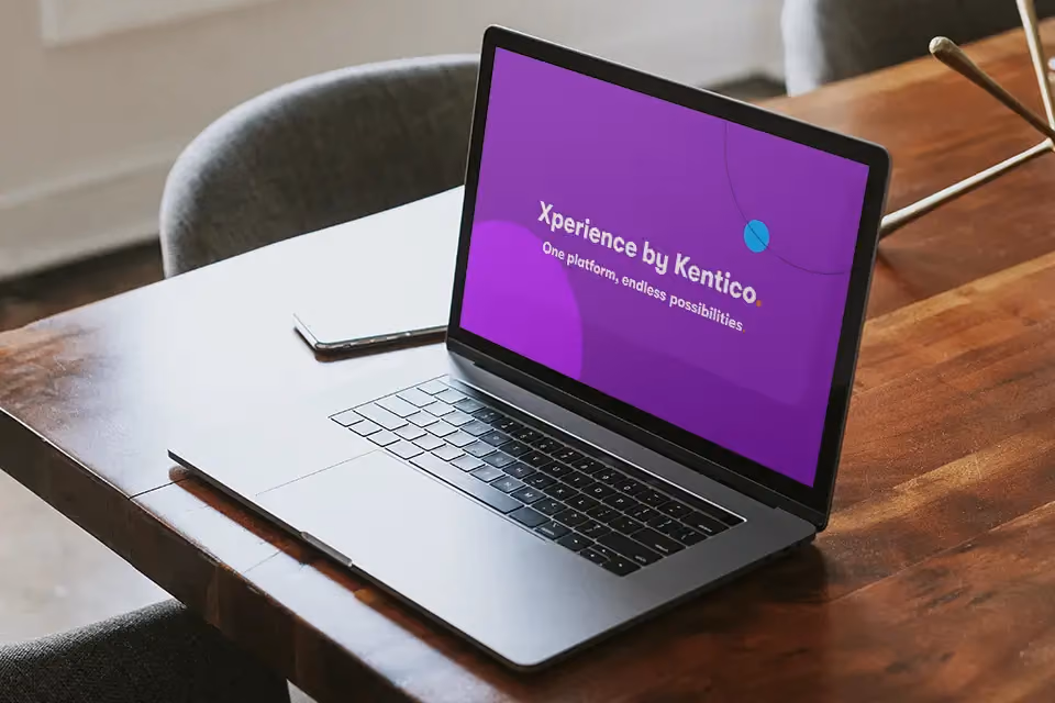 Open laptop on wooden table displaying purple screen with text 'Xperience by Kentico One platform, endless possibilities.'
