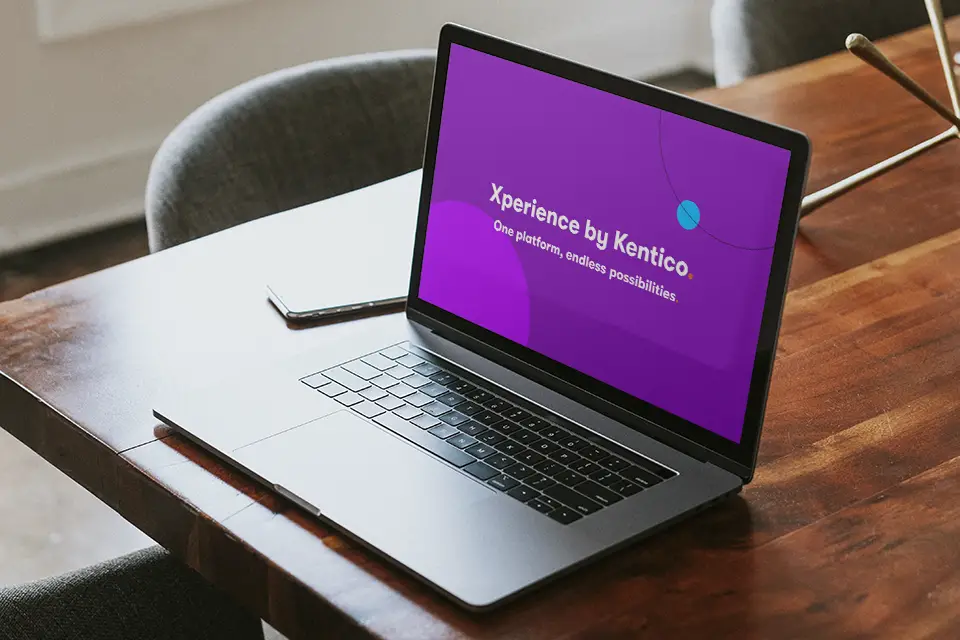 Open laptop on wooden table displaying purple screen with text 'Xperience by Kentico One platform, endless possibilities.'