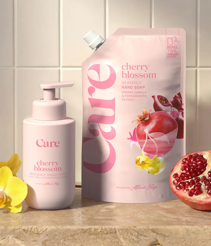 Pink bottle and refill pouch of Care cherry blossom hand soap with cherry, vanilla, and pomegranate extract on tiled countertop next to yellow flowers and half a pomegranate.