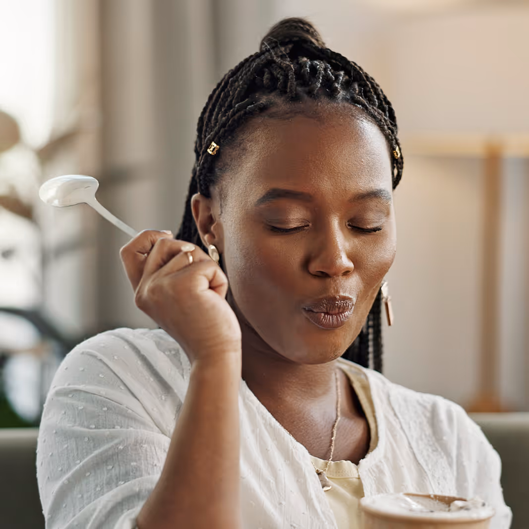 Woman with braided hair enjoying a spoonful of whipped coffee or dessert, eyes closed in a satisfied expression.