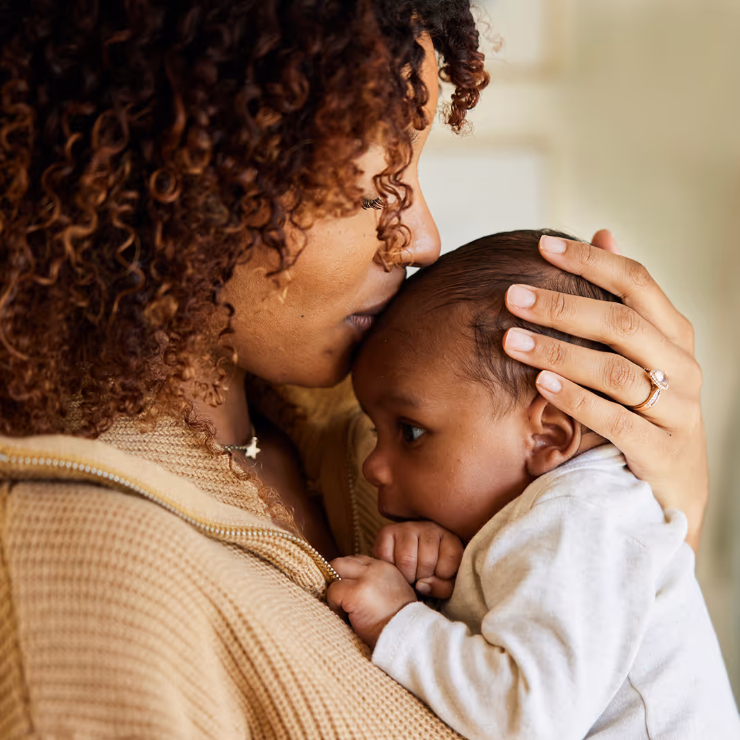Mother with curly hair gently kissing and holding her baby close.
