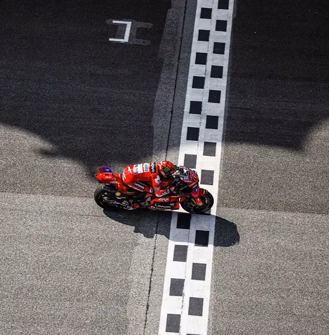 Motorcycle racer crossing the finish line on a red racing bike on a racetrack.