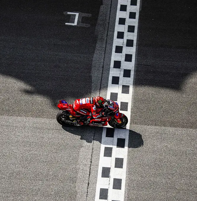 Motorcycle racer crossing the finish line on a red racing bike on a racetrack.