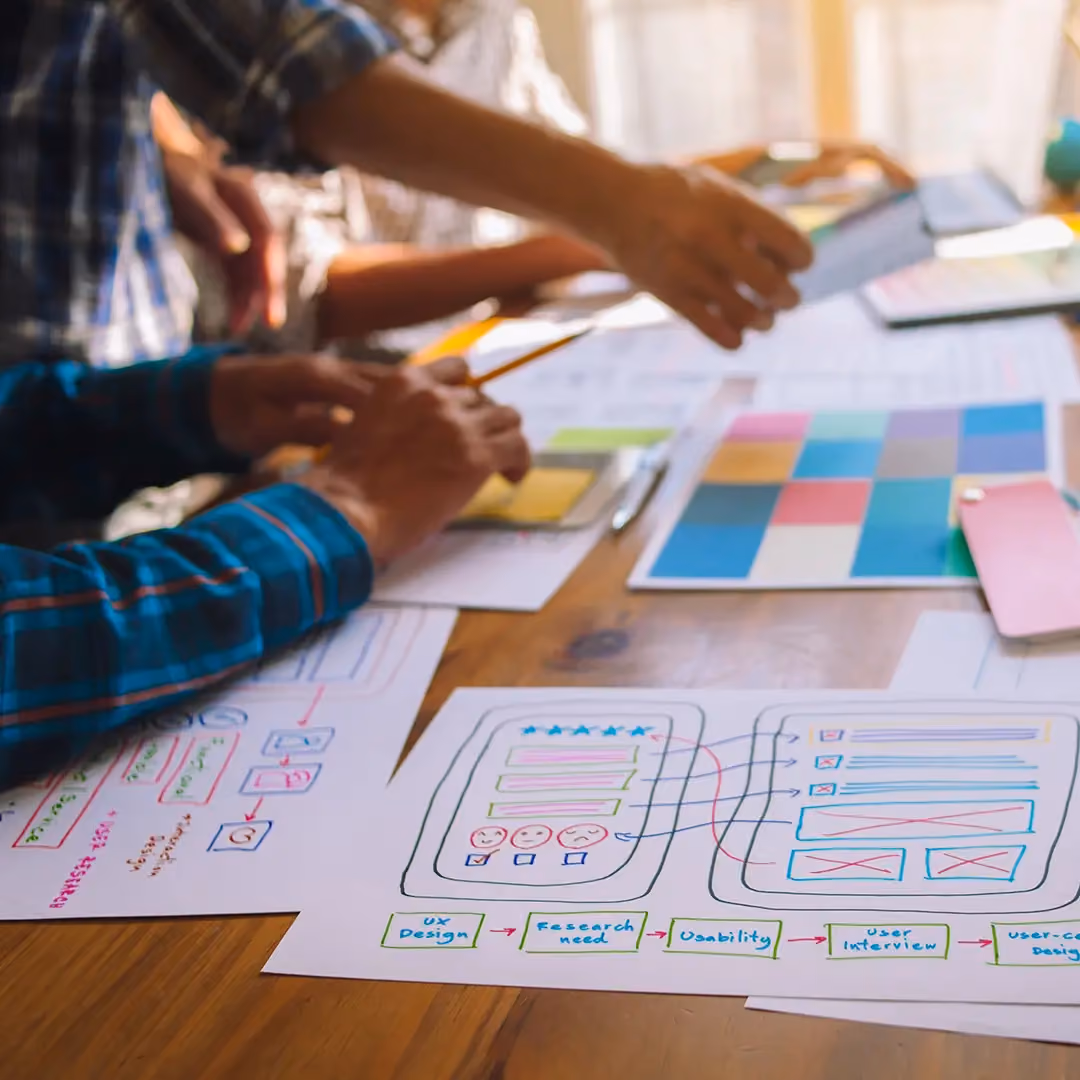 Close-up of hands working on user-centered design sketches and color swatches on a wooden table.
