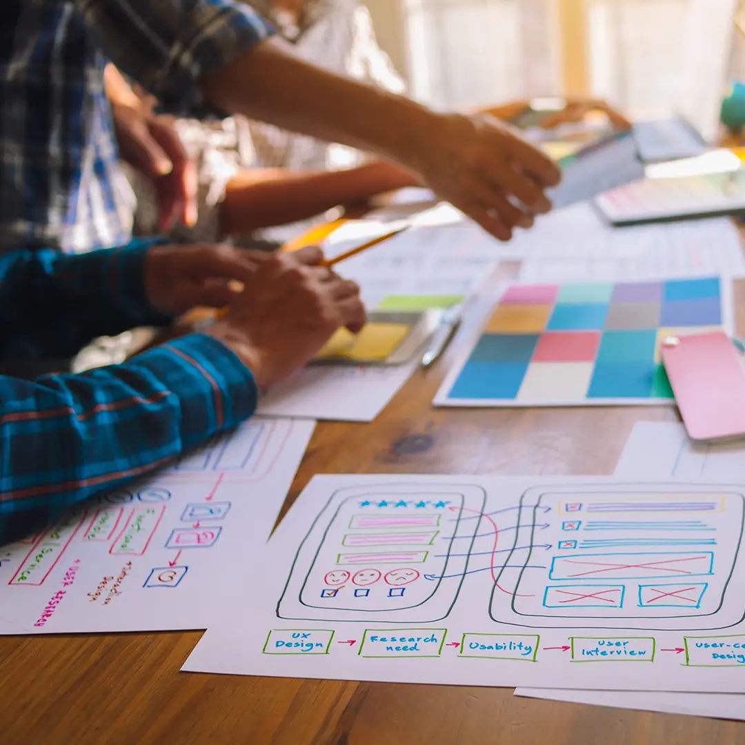 Close-up of hands working on user-centered design sketches and color swatches on a wooden table.