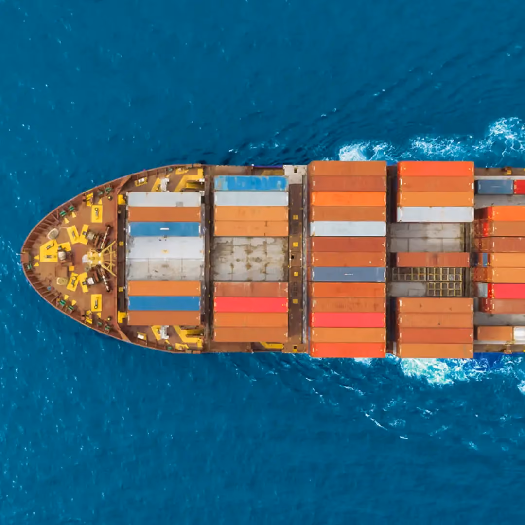 Aerial view of the bow of a cargo ship loaded with multicolored shipping containers sailing in blue ocean water.