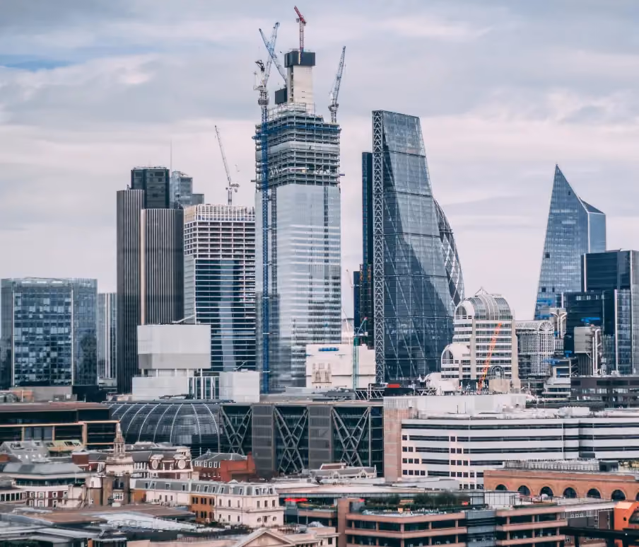 City skyline featuring modern skyscrapers under construction with cranes against a cloudy sky.