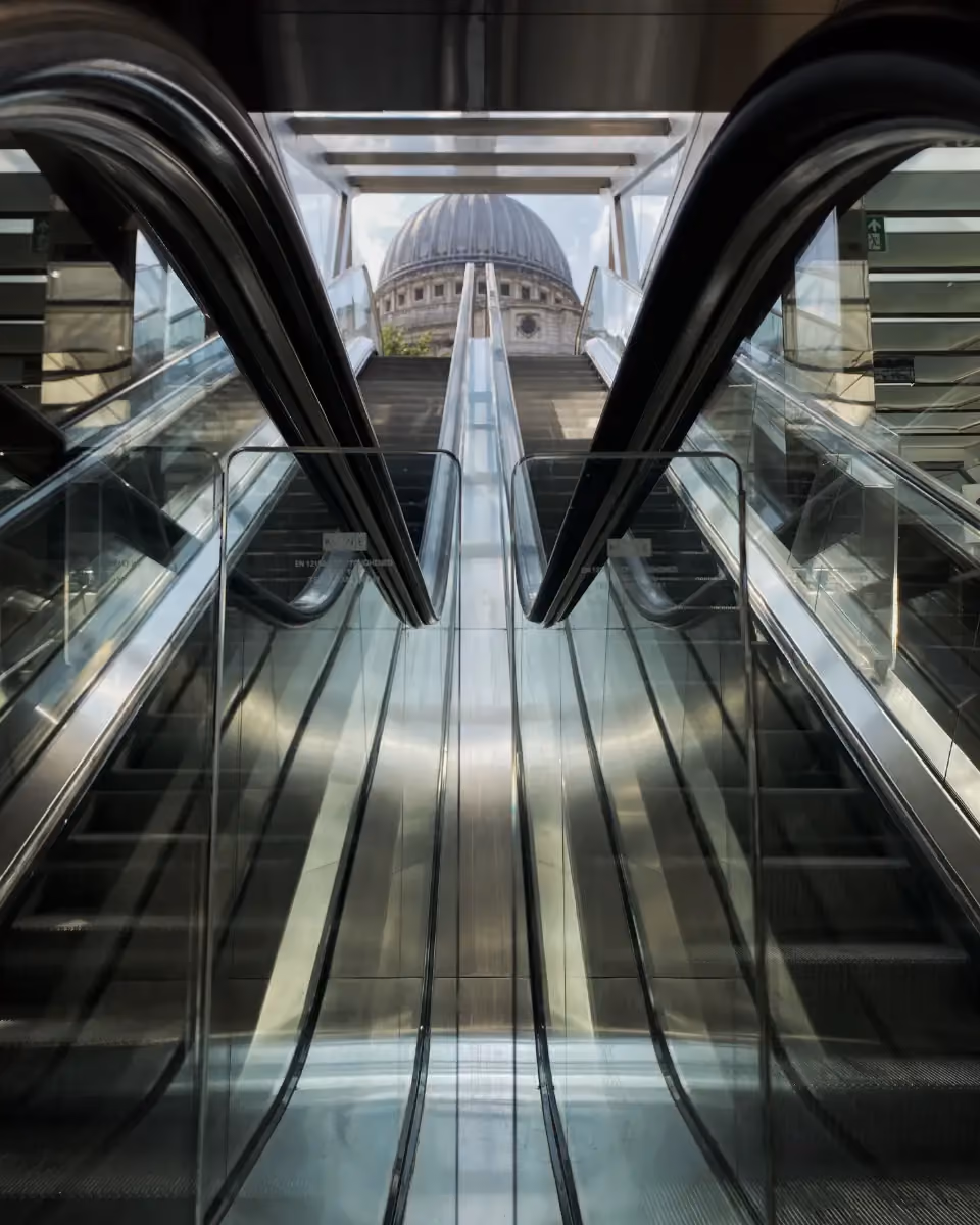 Upside view of glass escalators leading up to a dome-shaped building in the background.