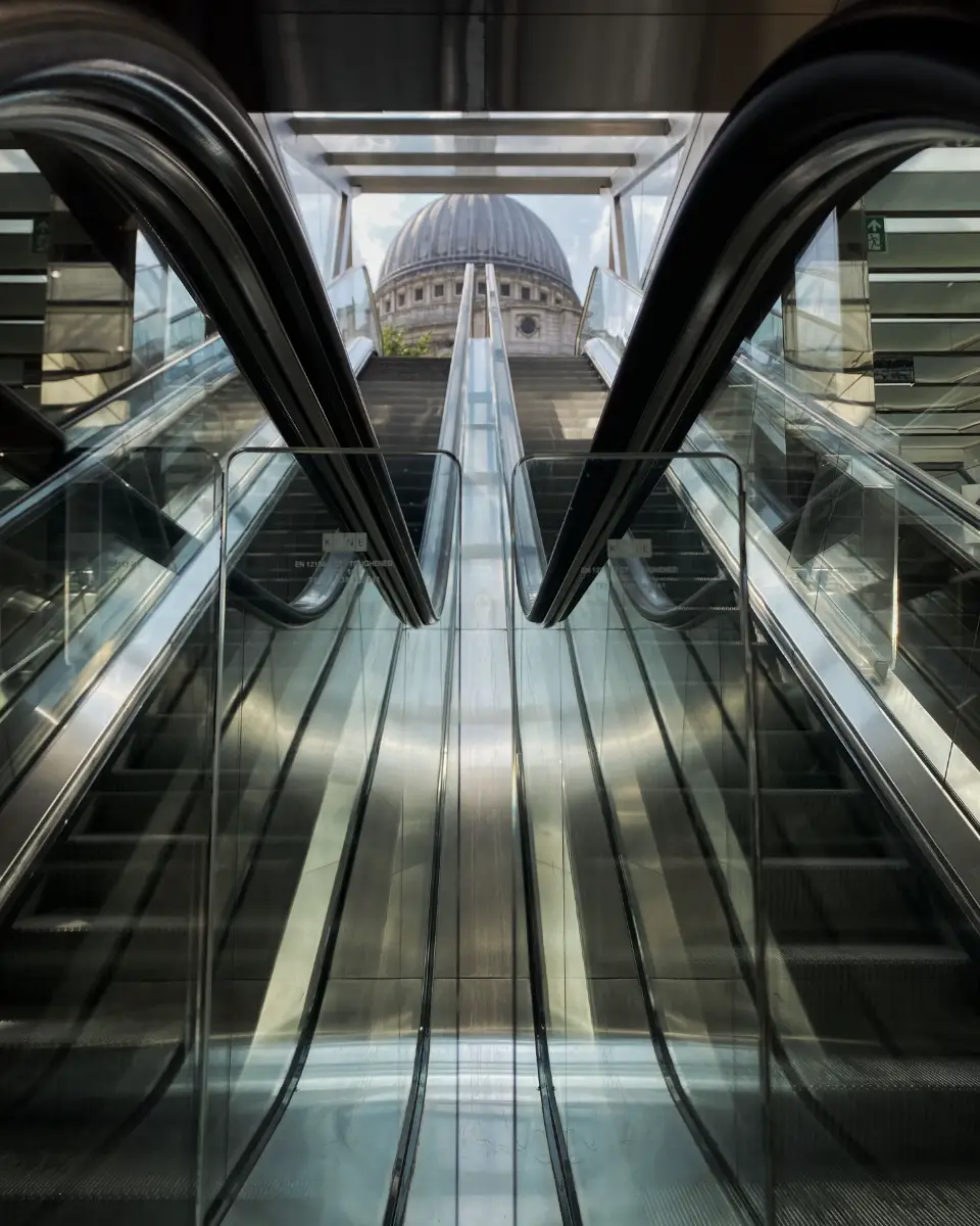 Upside view of glass escalators leading up to a dome-shaped building in the background.