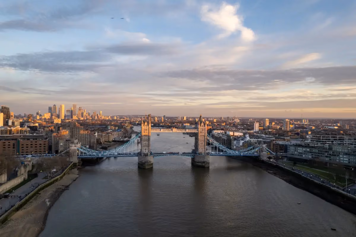 View of Tower Bridge across the River Thames with London skyline in the background at sunset.