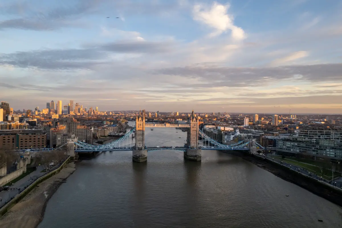 View of Tower Bridge across the River Thames with London skyline in the background at sunset.