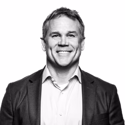 Smiling middle-aged man in a suit jacket and open-collar shirt against a white background.