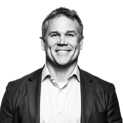 Smiling middle-aged man in a suit jacket and open-collar shirt against a white background.