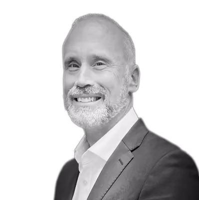 Smiling middle-aged man with white beard in a dark suit and white shirt against a black background.