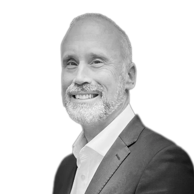 Smiling middle-aged man with white beard in a dark suit and white shirt against a black background.