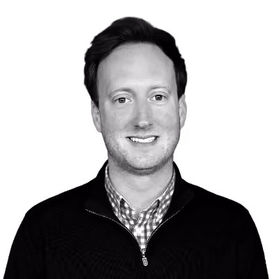 Smiling man with short hair wearing a checkered shirt and dark zip-up sweater.