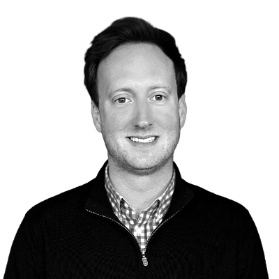 Smiling man with short hair wearing a checkered shirt and dark zip-up sweater.