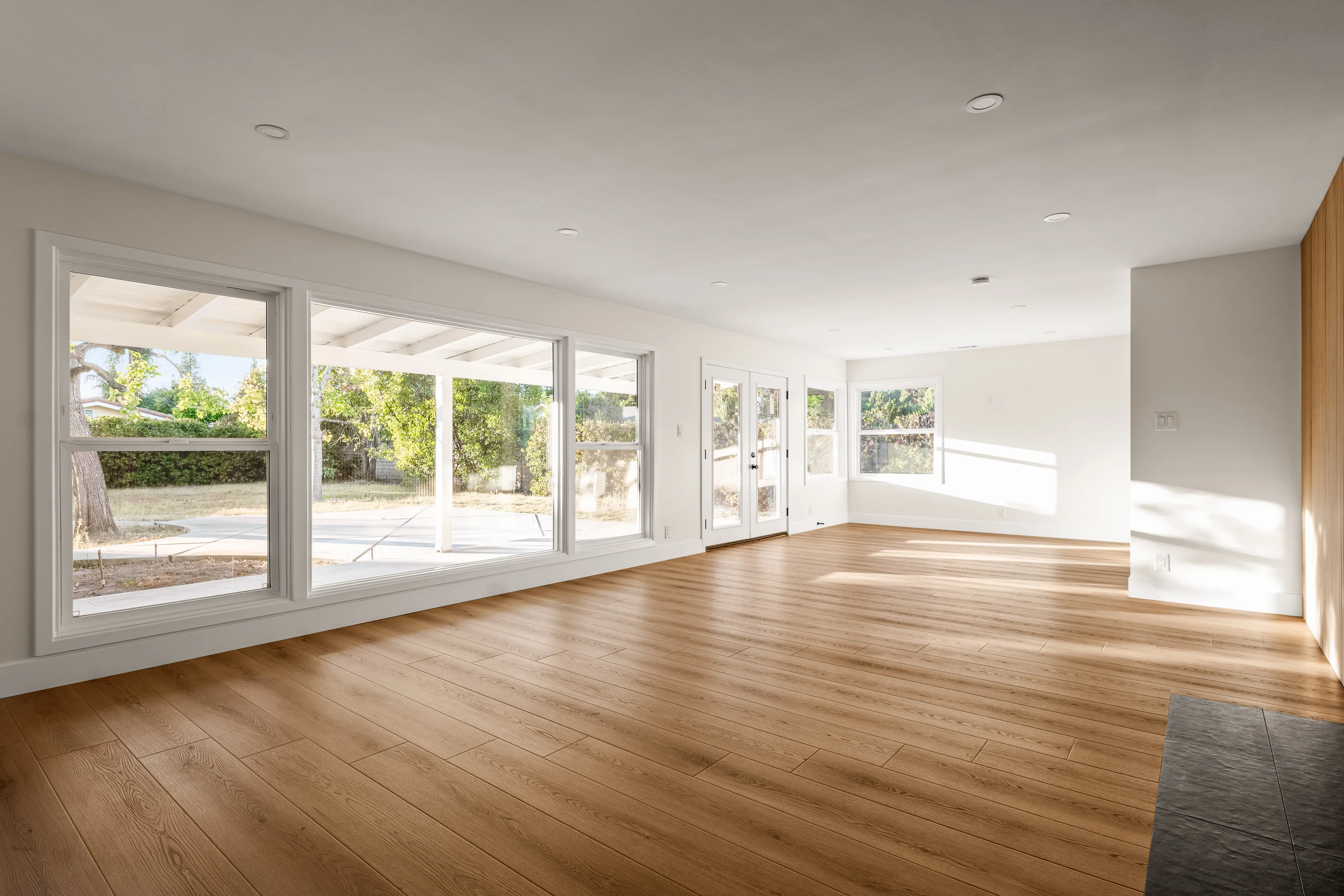 Open living room with wall of windows, white walls, and wide-plank oak floors facing the backyard.