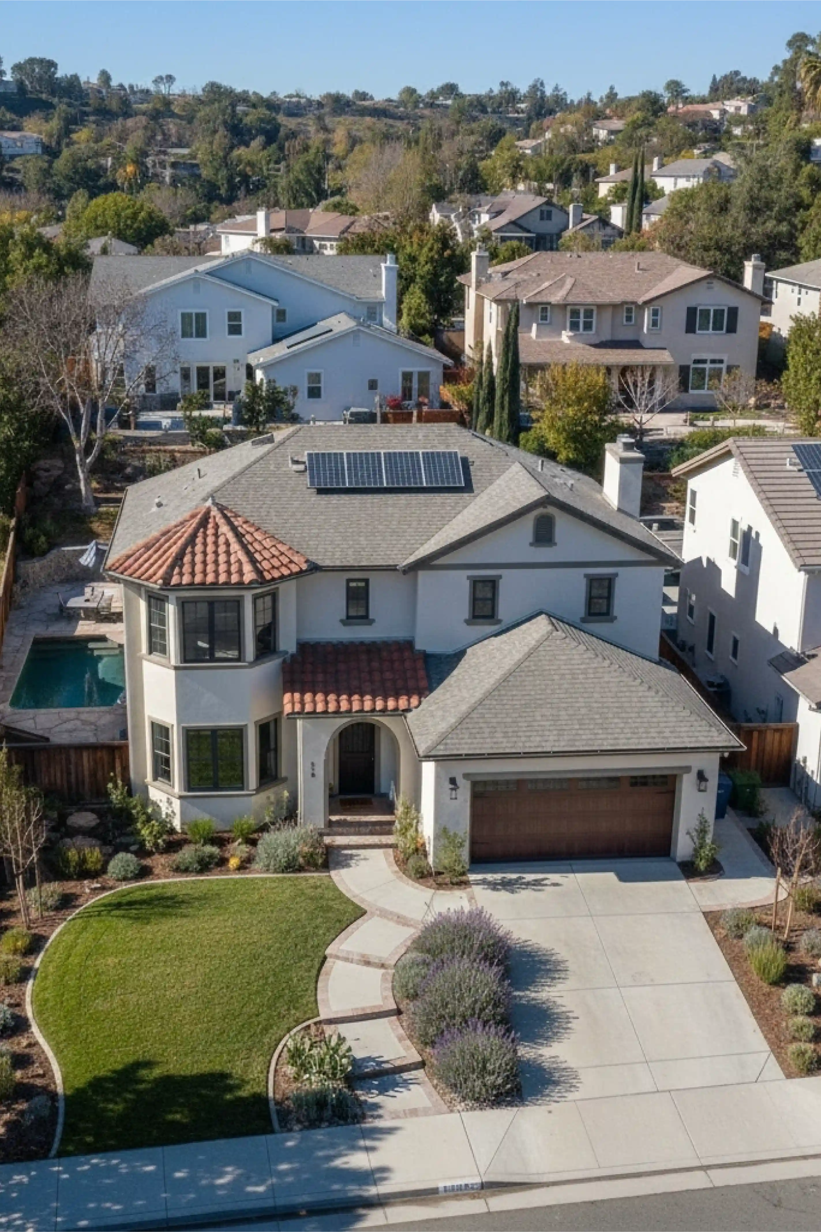 Two-story suburban house with solar panels on the roof, a curved walkway, and landscaped front yard with bushes and grass.