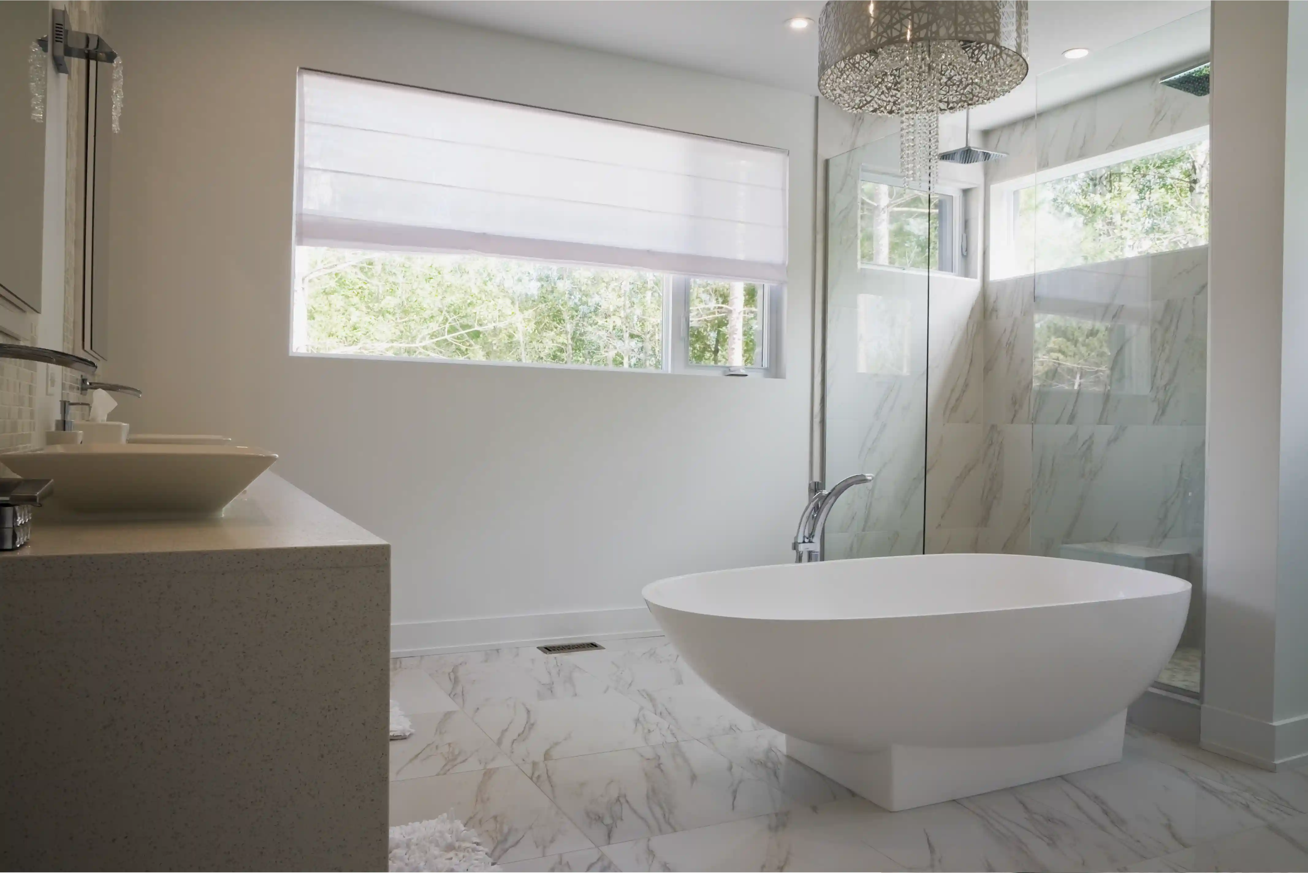 Modern bathroom with a freestanding white bathtub, marble floor tiles, glass shower enclosure, and a large window with white blinds.