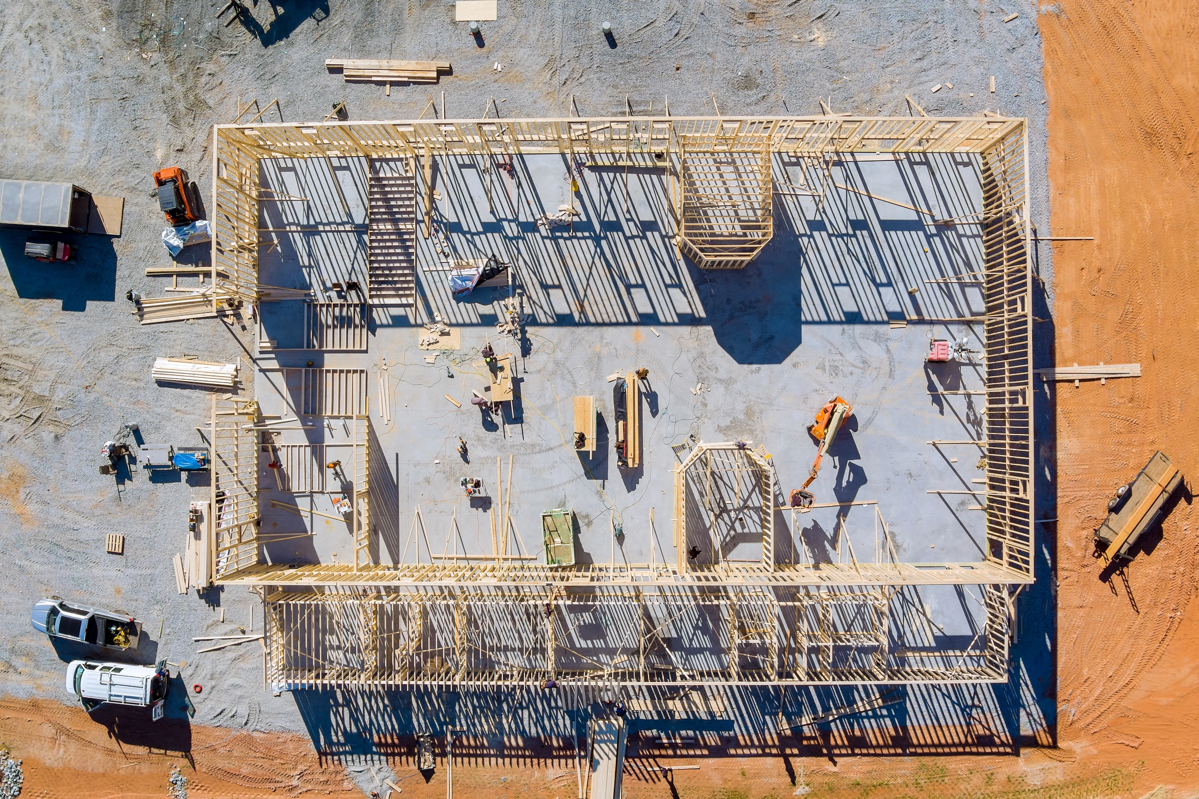 Aerial view of a wooden frame construction of a building on a concrete slab with workers and equipment.