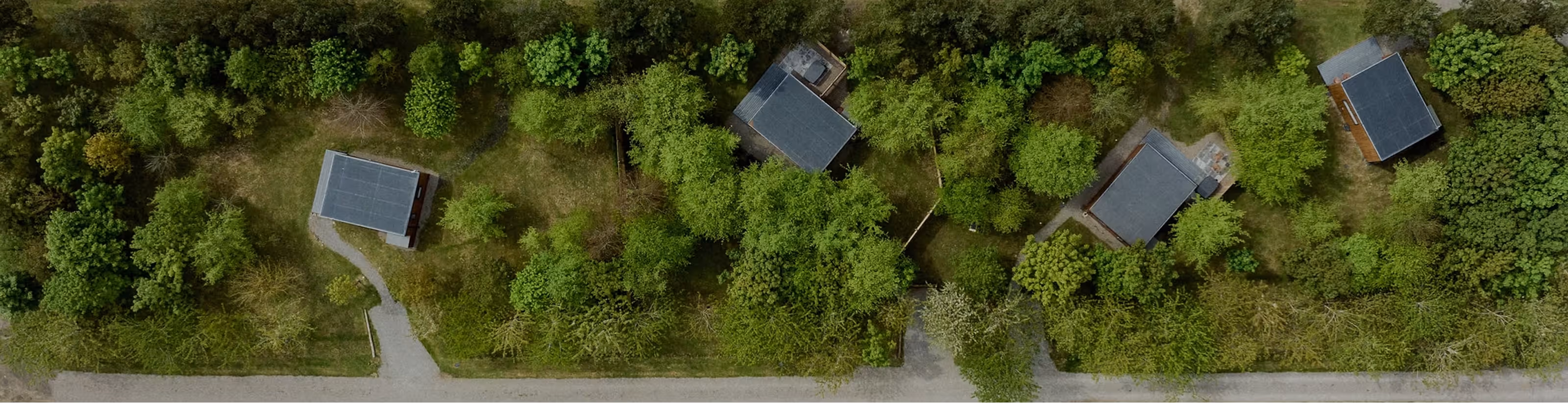 Aerial view of five small houses surrounded by dense green trees and connected by curved paths.