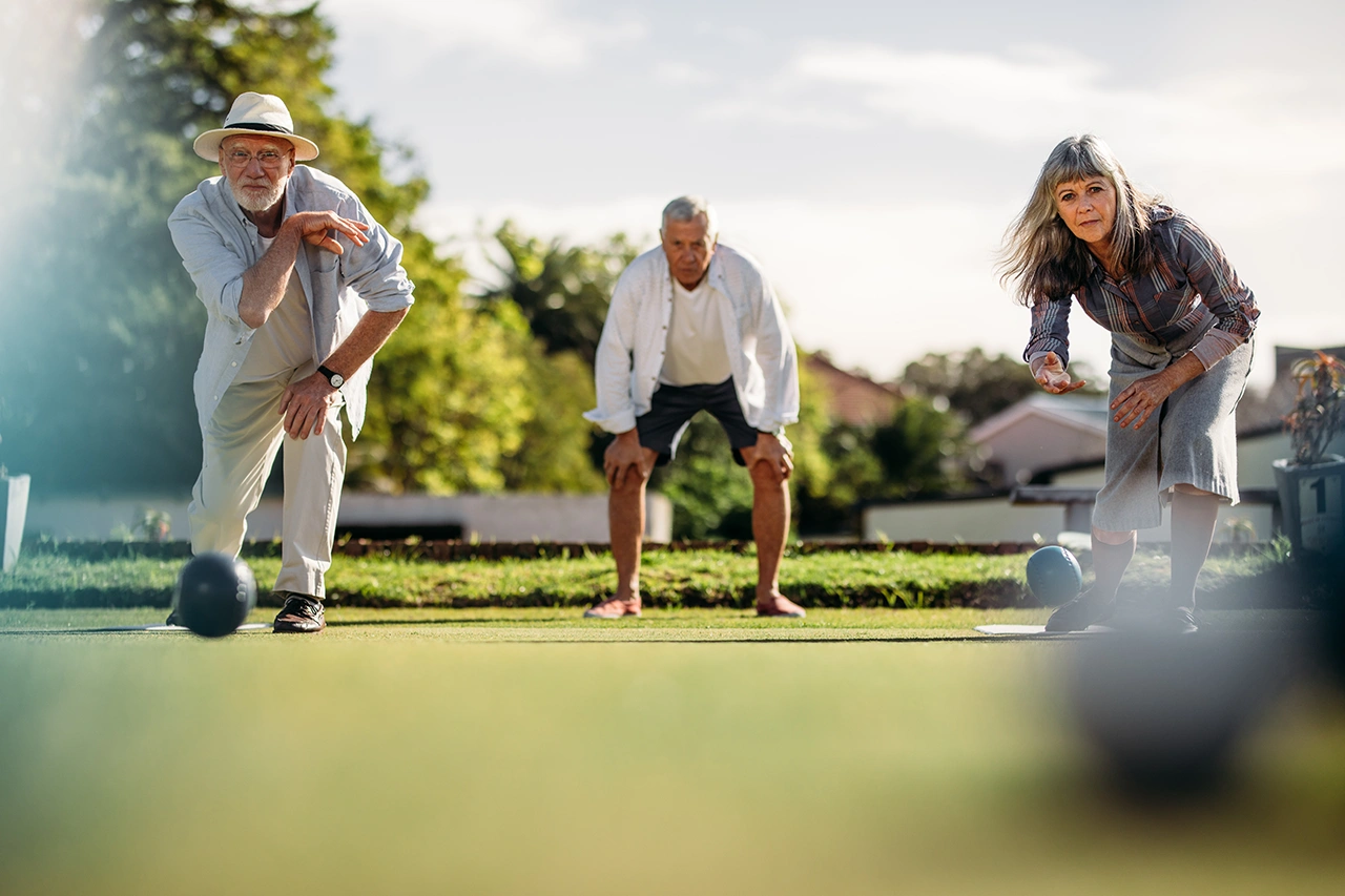 Three seniors playing bocce ball outdoors on a sunny day.