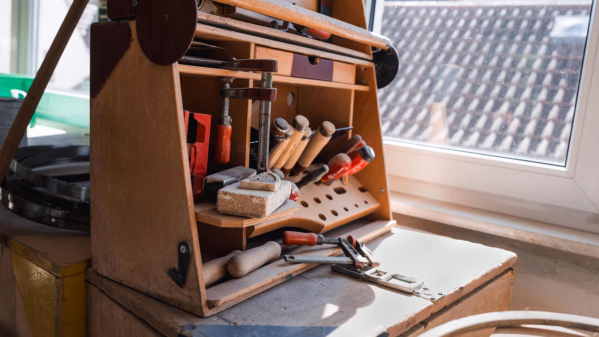 Holz Werkzeugkasten mit verschiedenen Handwerkzeugen neben einem Fenster mit Dachansicht.