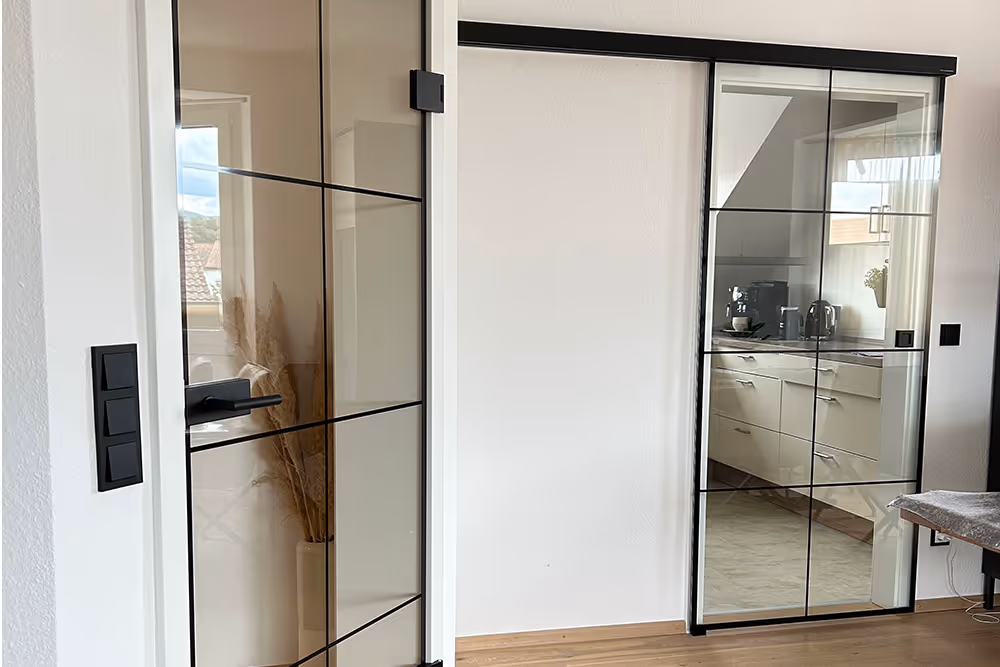 Moderner Innenraum mit zwei schwarzen Glas-Türen, eine Schiebetür zur Küche und eine geöffnete Tür zum anderen Raum.