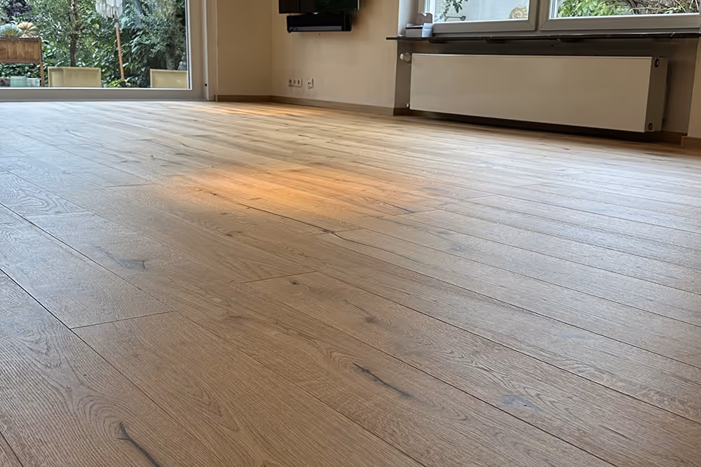 Heller Holzfußboden in einem leeren Raum mit großen Fenstern und Blick auf einen Garten.