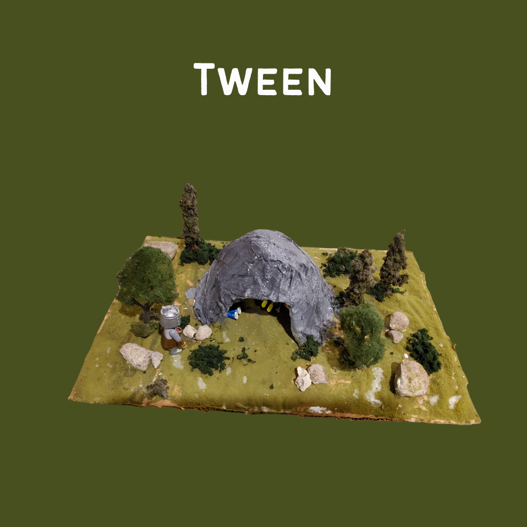 Model diorama of a gray cave surrounded by trees and rocks on green ground with the word 'TWEEN' above it.