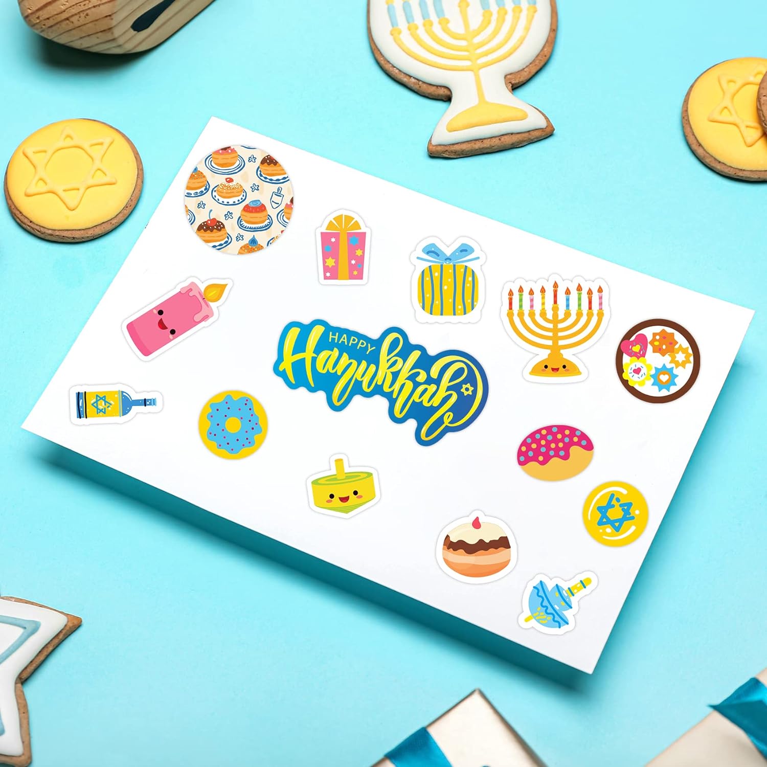 Sheet of colorful Hanukkah-themed stickers on a white box including menorah, dreidel, doughnuts, presents, candles, and 'Happy Hanukkah' text.
