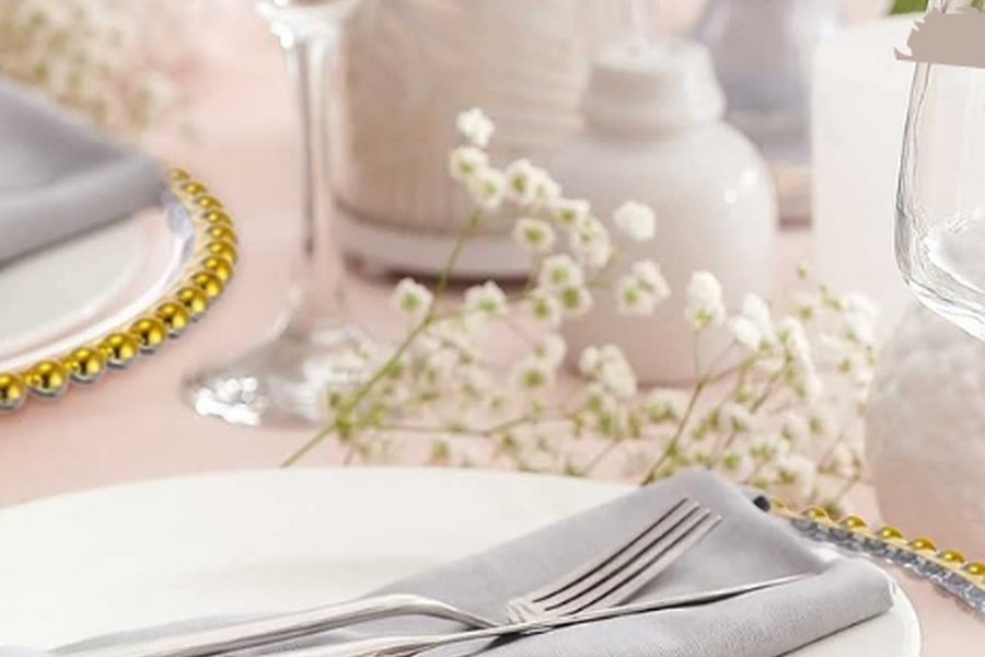 Tablescapes — a set table with gold-beaded glass chargers, folded grey napkins, glassware and baby’s breath.