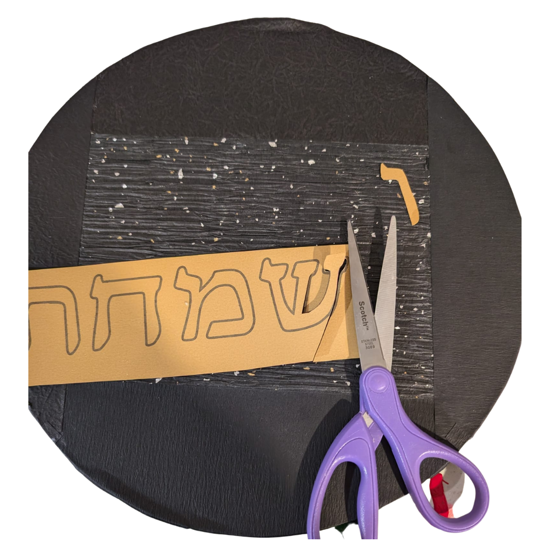 The Hebrew phrase cut from gold paper with scissors on the black circle