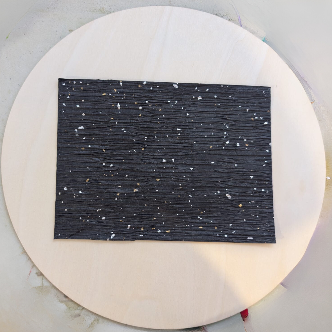 A black speckled rectangle of decoupage paper glued to the centre of a round wooden disc