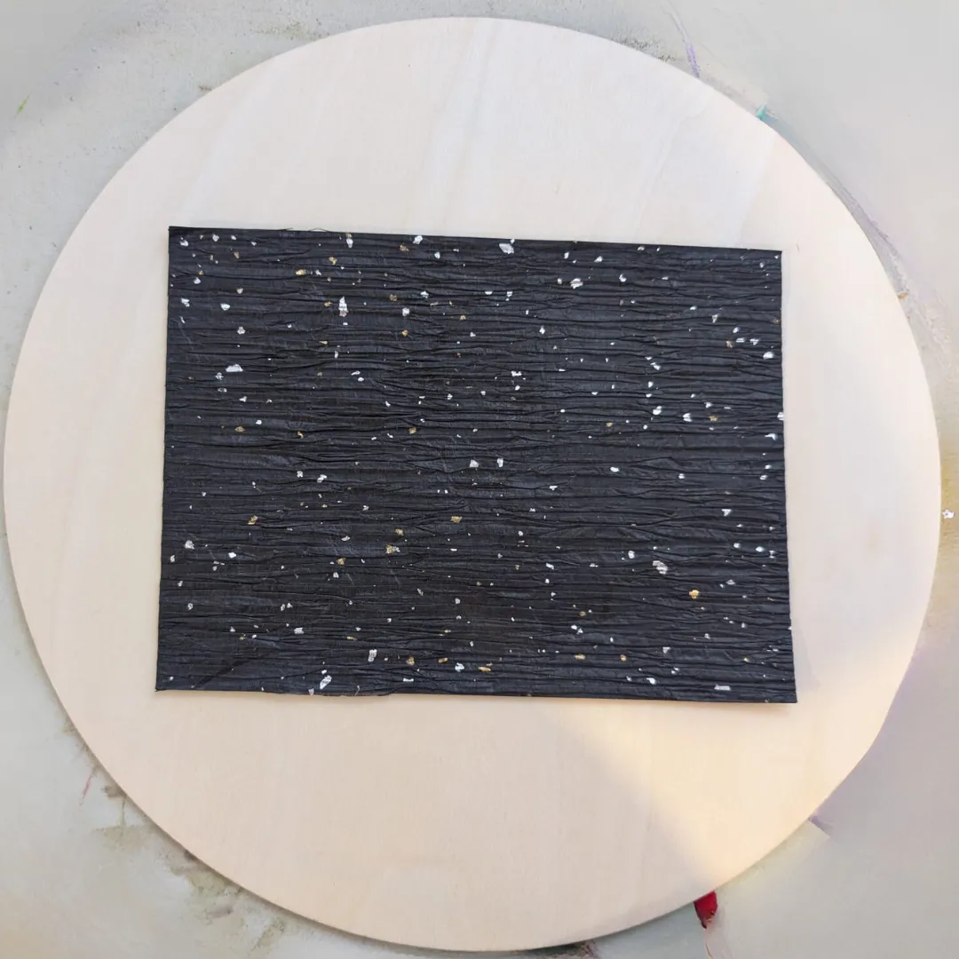A black speckled rectangle of decoupage paper glued to the centre of a round wooden disc