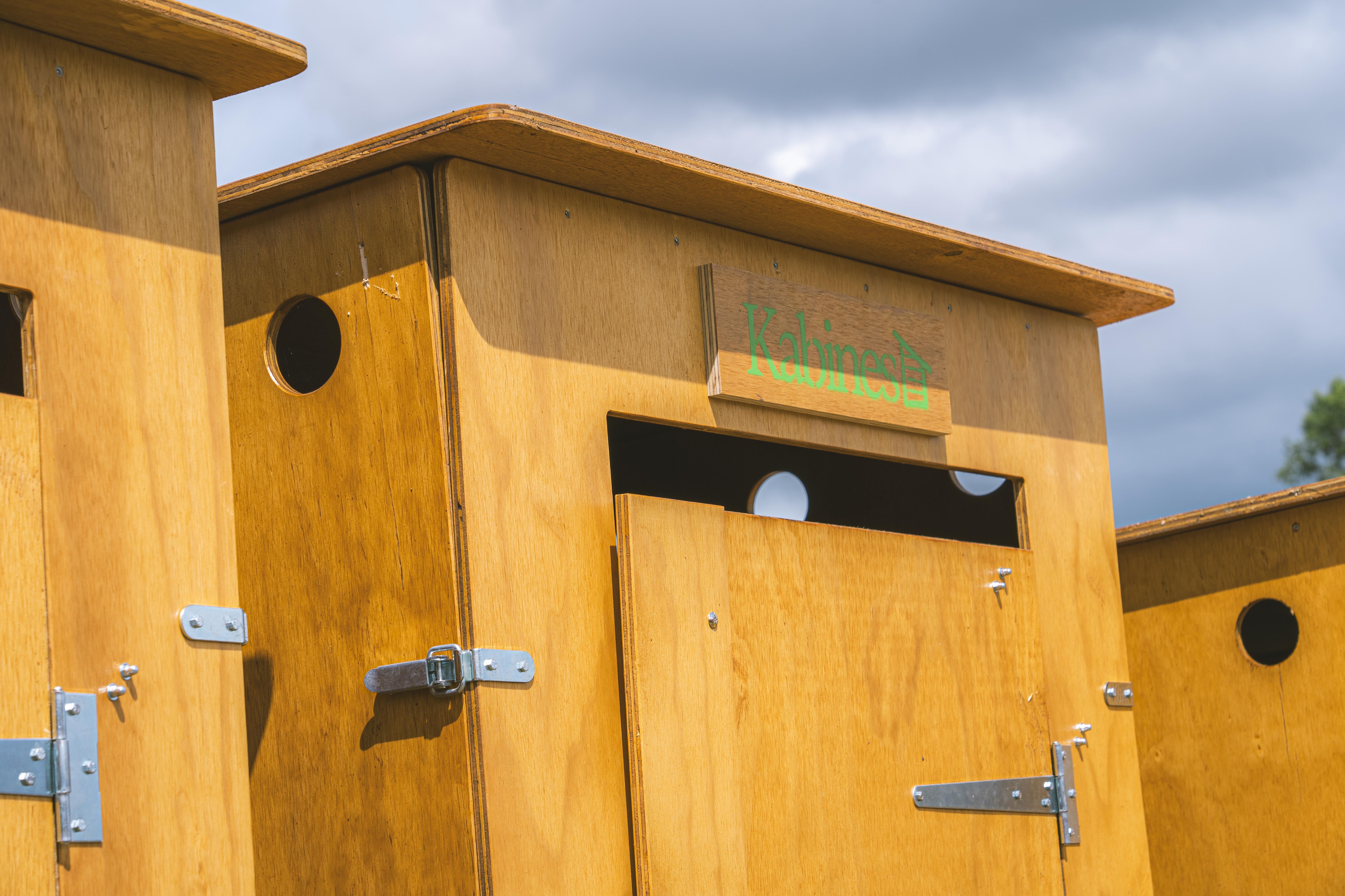 Plusieurs cabines en bois clair avec petites ouvertures circulaires sous un ciel nuageux.