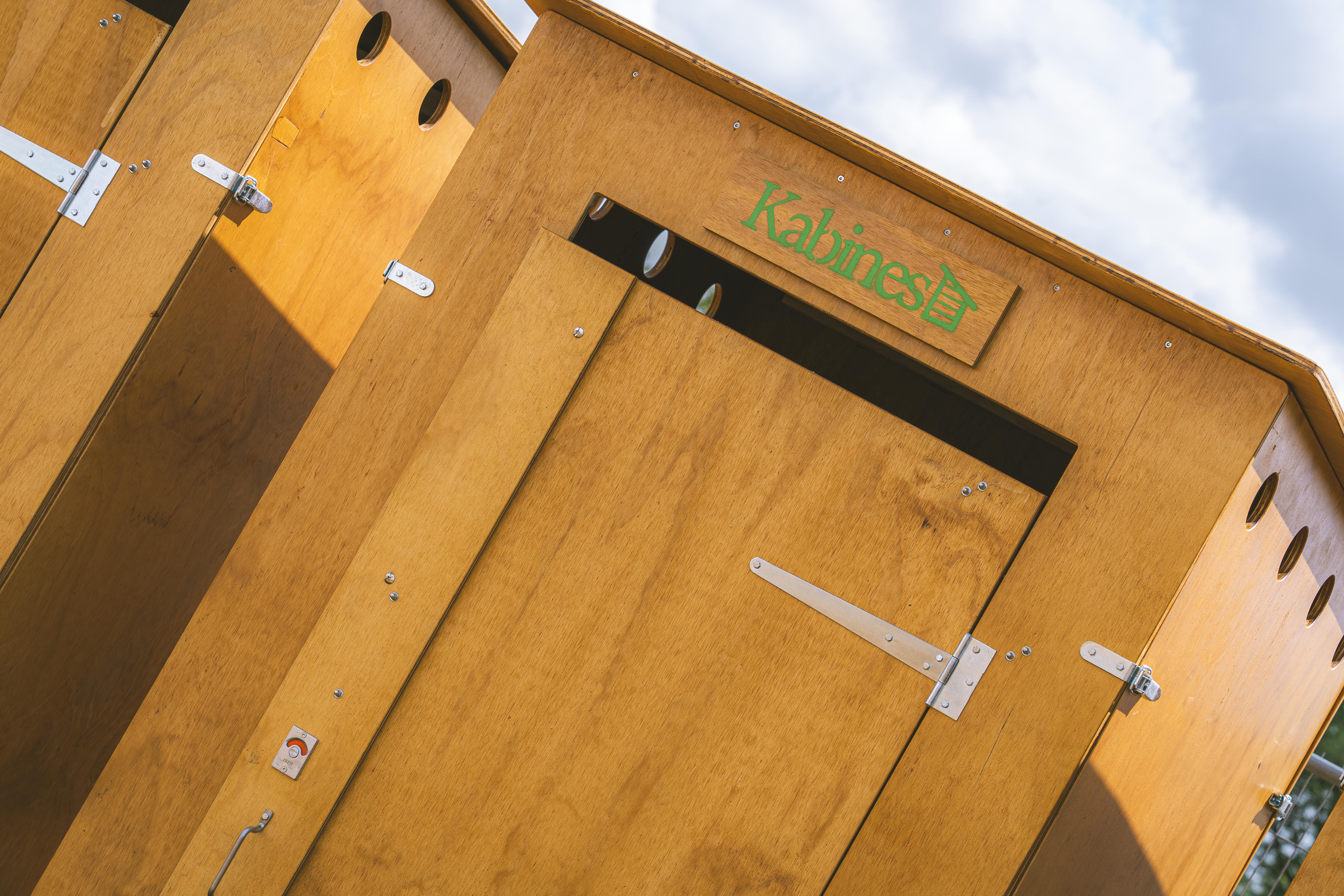 Cabines en bois claires avec panneaux et poignées métalliques sous un ciel partiellement nuageux.