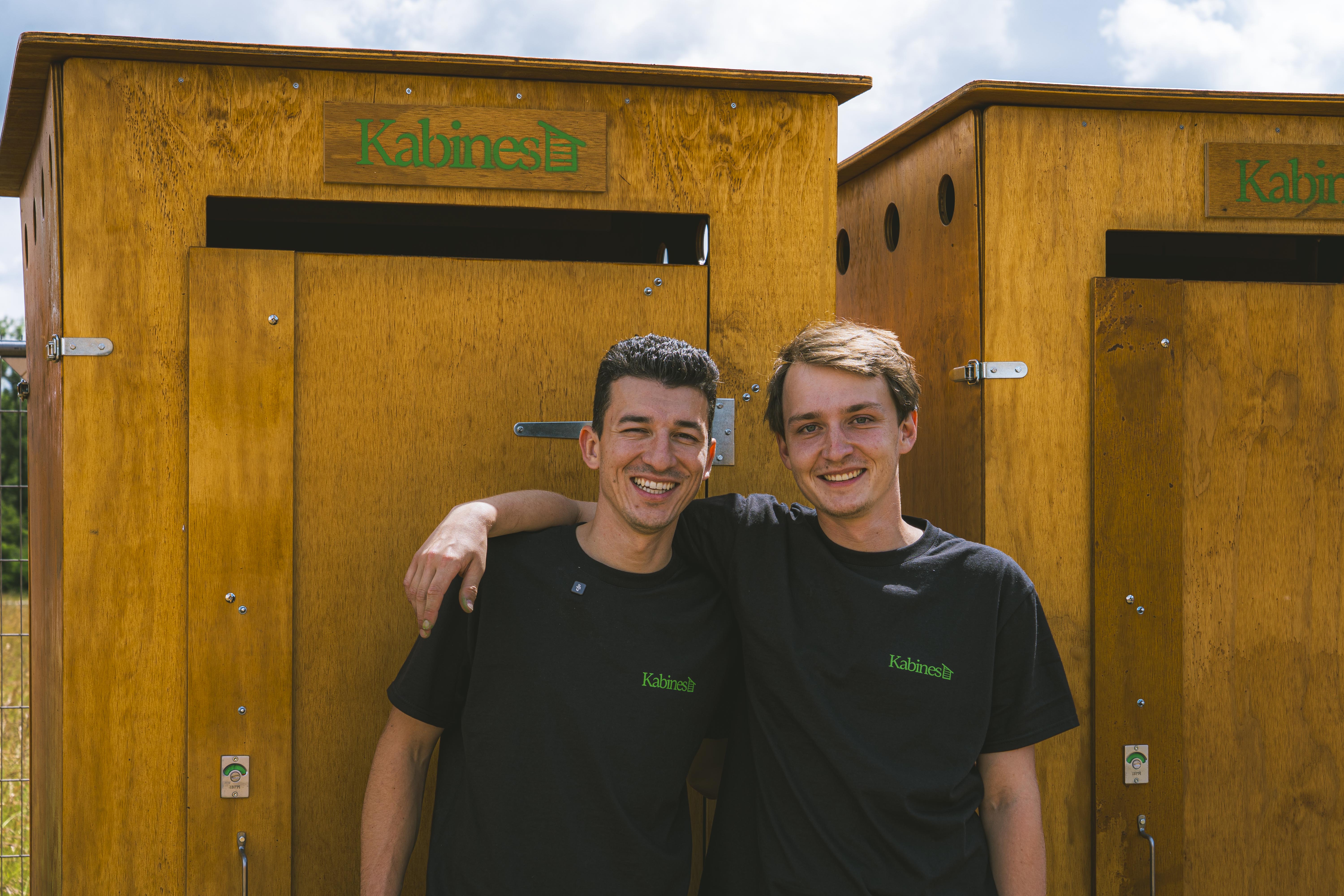 Deux hommes souriants en t-shirts noirs avec logo Kabines devant des cabines en bois.