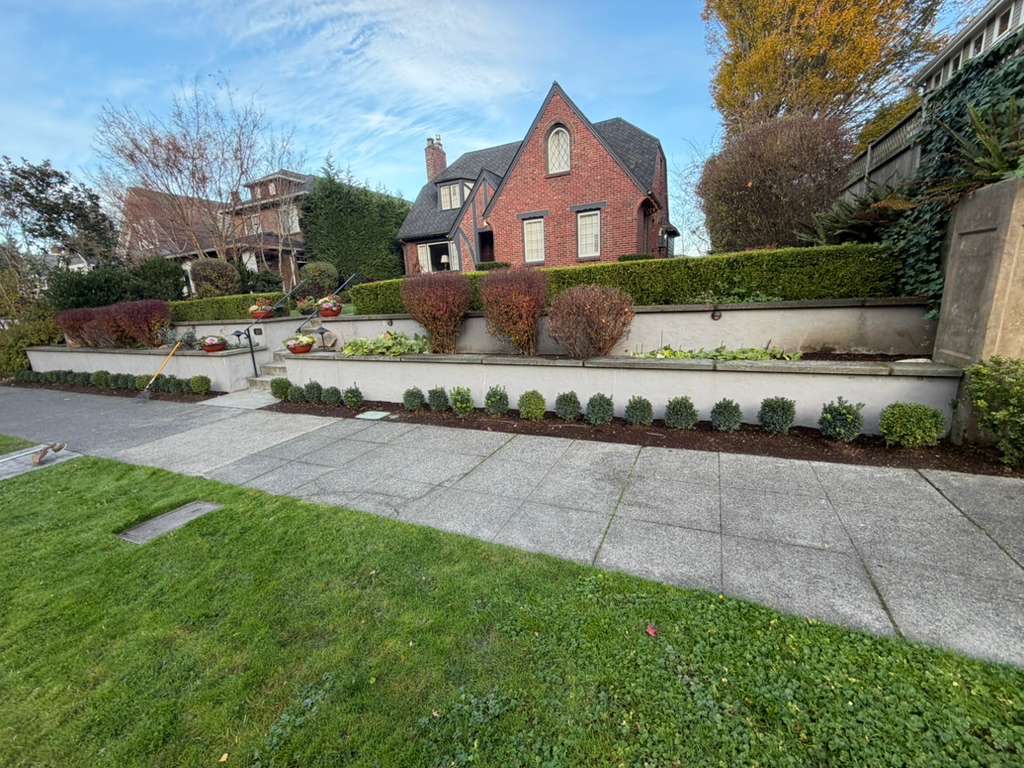 Brick house behind a tiered garden with trimmed bushes and a stone walkway in front.