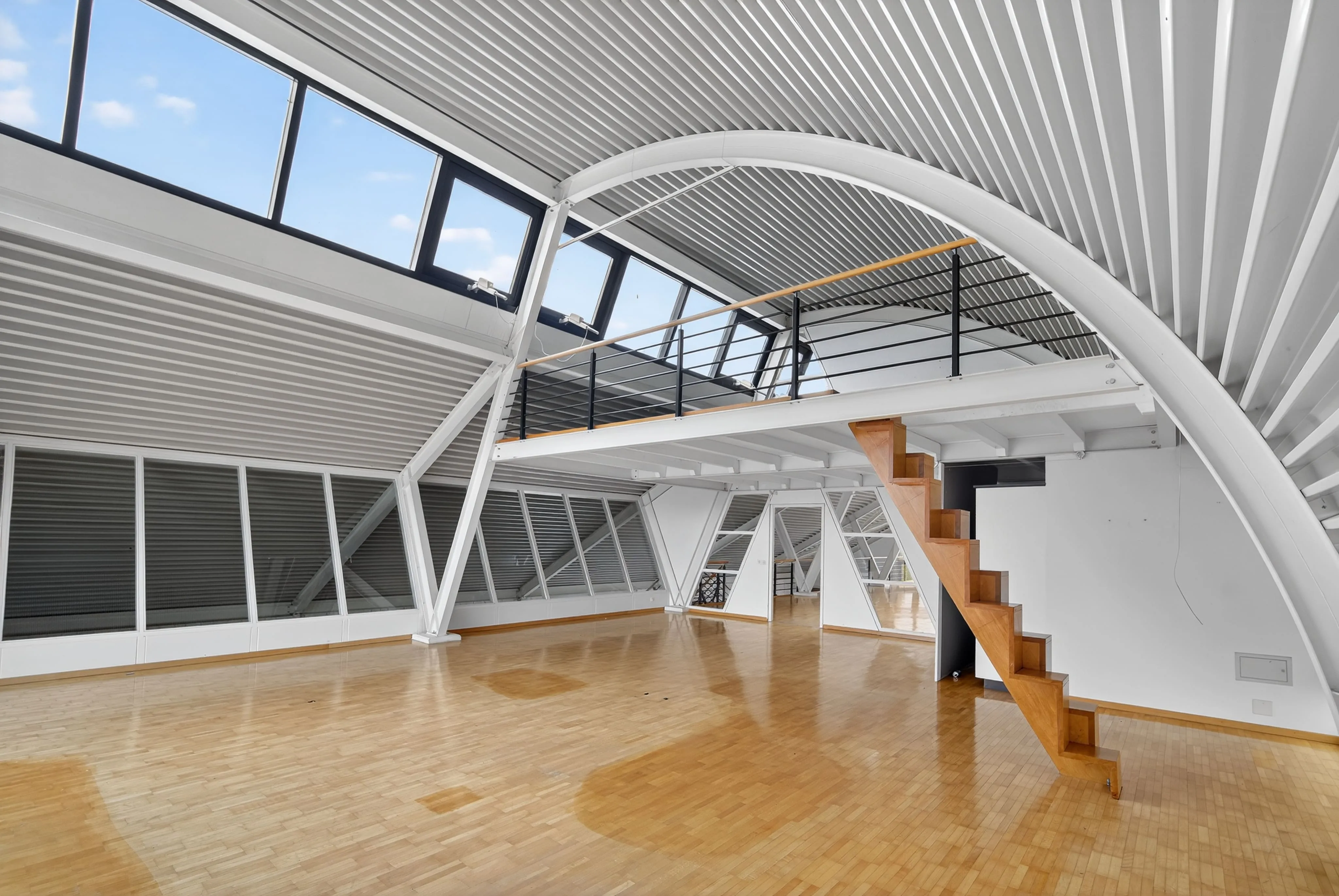 Modern loft apartment with large windows, wooden staircase, and light hardwood floors.