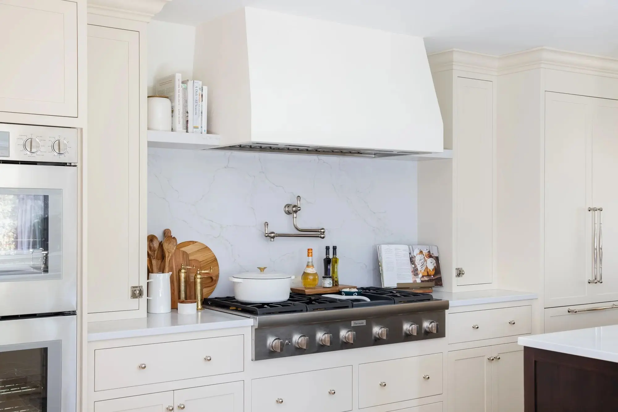 Modern kitchen with a stainless steel six-burner stove, white cabinetry, marble backsplash, and wooden kitchen utensils on the counter.