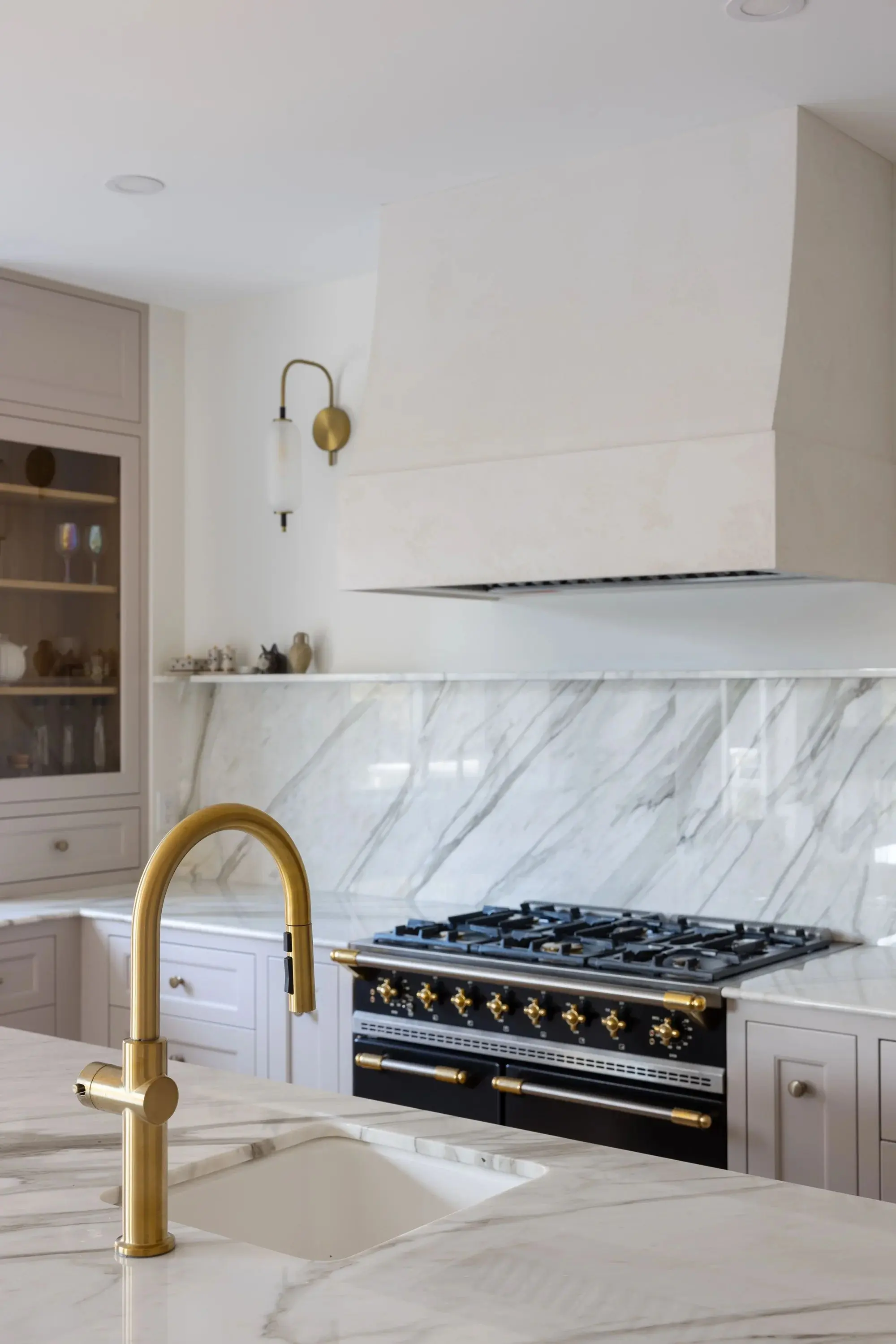 Modern kitchen featuring a brass faucet over a marble countertop, with a black stove and marble backsplash in the background.