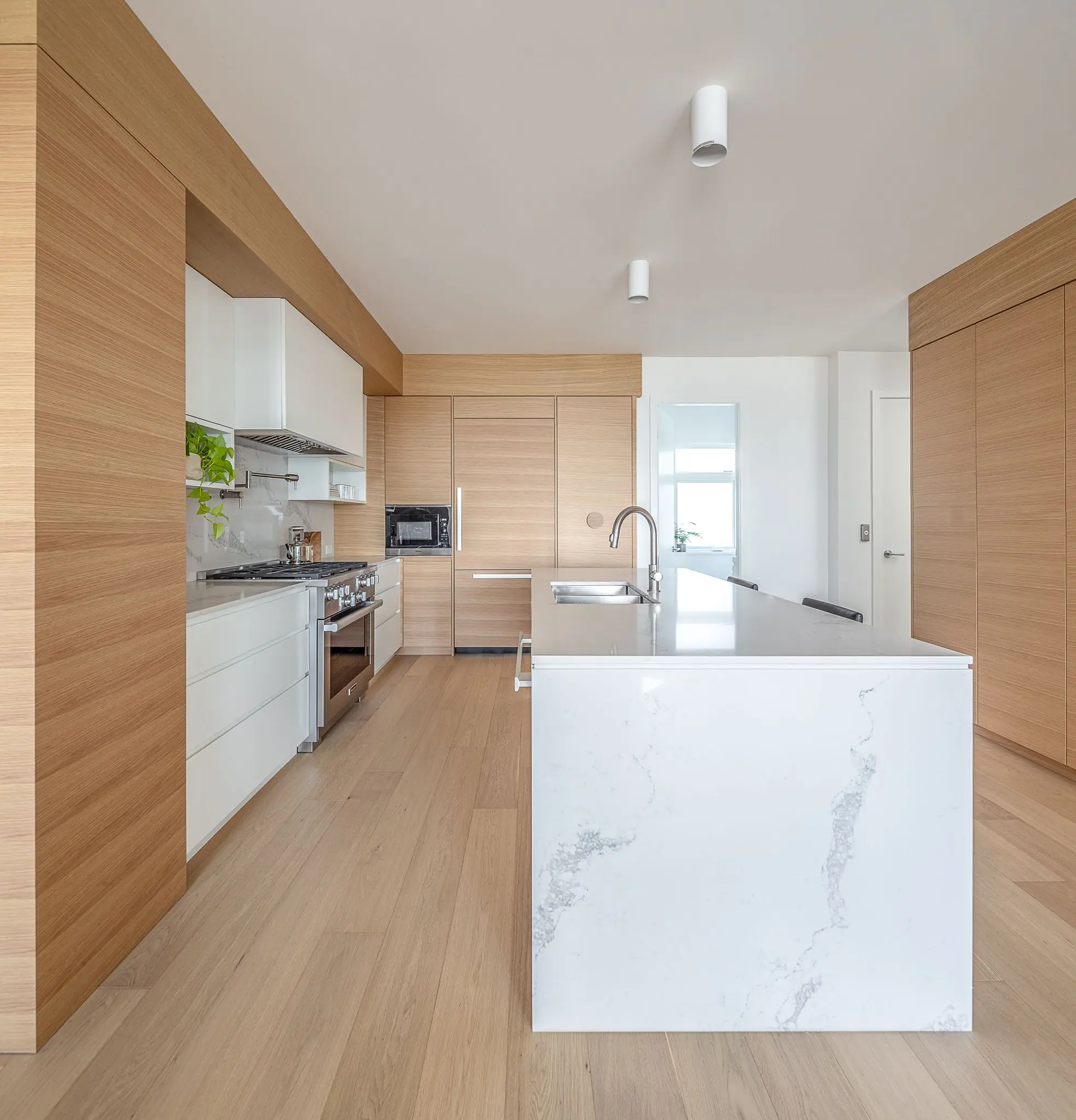 Modern kitchen with white marble island, wooden cabinetry, stainless steel stove, and built-in microwave.