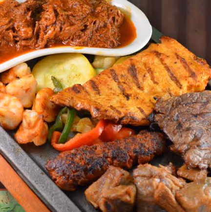 A platter featuring grilled steak, chicken, and sausage, accompanied by shrimp, vegetables, and shredded beef in sauce.