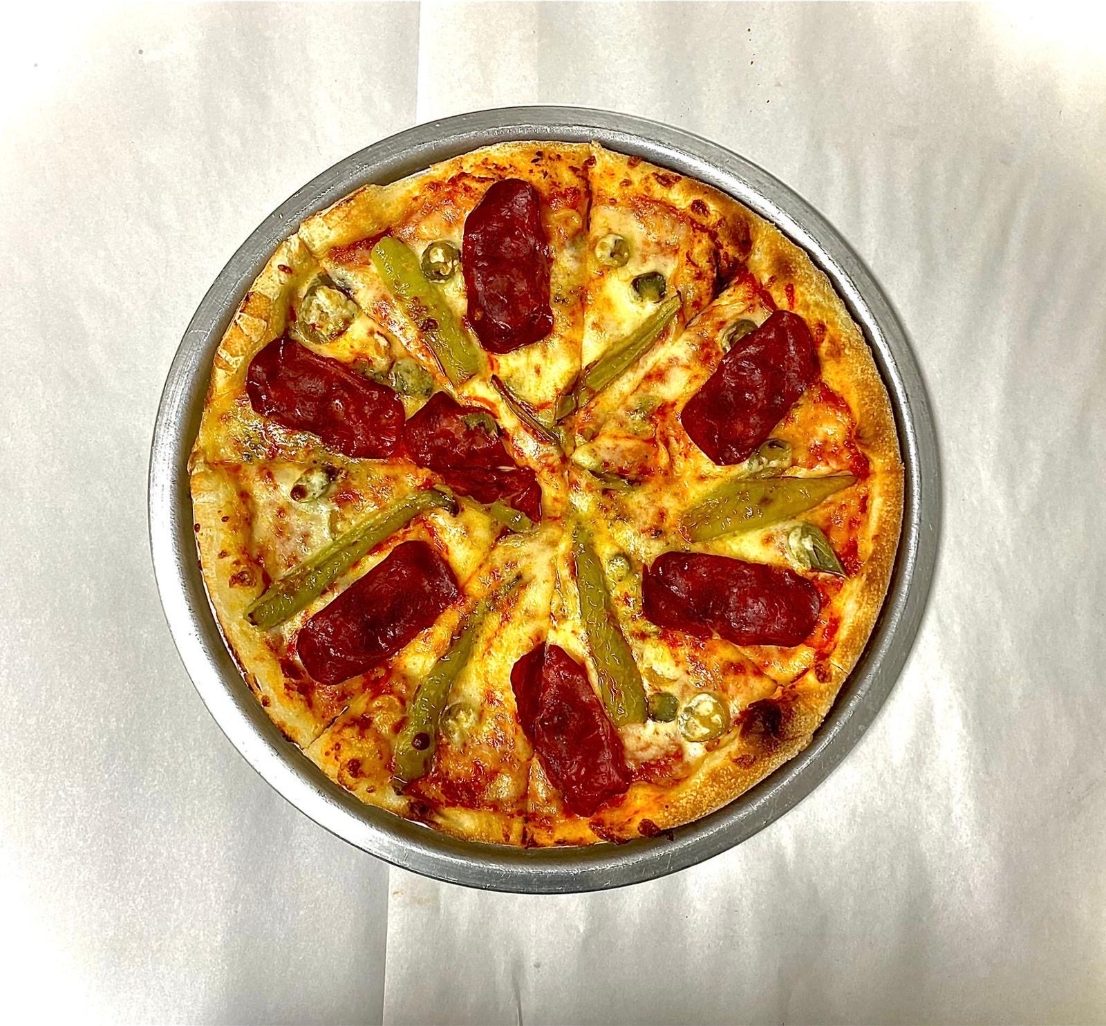 Whole pepperoni pizza topped with green chili peppers and sliced jalapeños in a round metal tray on white parchment paper.