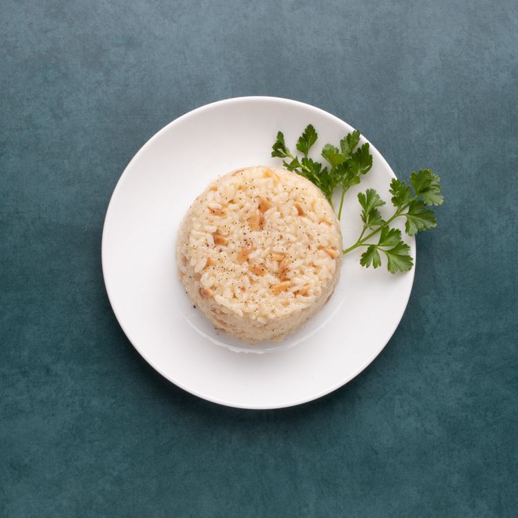 Plate of cooked rice mixed with small pieces of nuts, garnished with fresh parsley on the side.